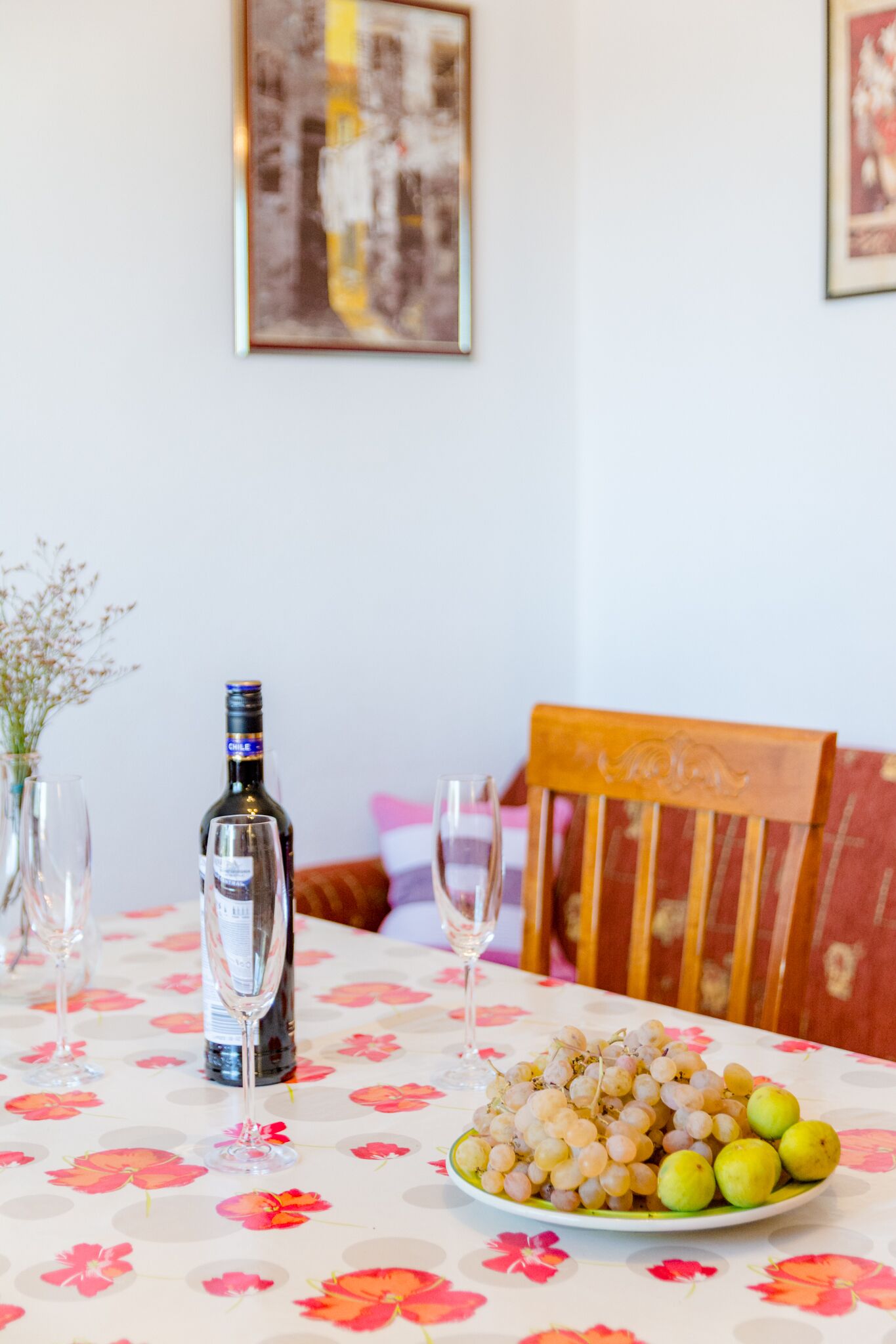 Una mesa de comedor con mantel floral, una botella de vino y un plato de uvas y limones.