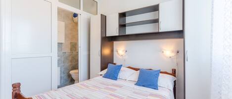 A bedroom with a bed, a wardrobe, a bathroom, and a small shelf unit.