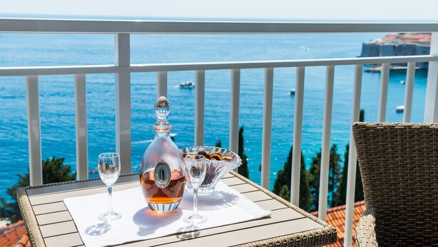 Mesa com garrafa e copos numa varanda com vista para o mar.