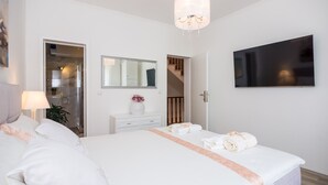 Ein Hotelzimmer mit einem großen Bett, einem an der Wand befestigten Fernseher, einem Spiegel, einem Nachttisch mit Lampe und einer Dusche.