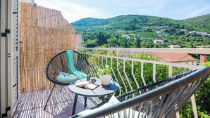 Ein Balkon mit Blick auf einen grünen Hang, ein Korbstuhl, ein kleiner Tisch mit einem Buch und Sonnenbrille sowie ein Bambuszaun.