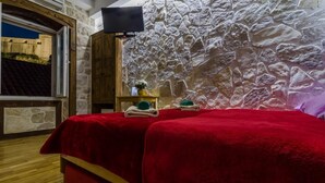 Una habitación con pared de piedra, un armario de madera, una cama con ropa de cama roja y una pequeña mesa con un florero y toallas.