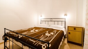 Un lit simple avec un cadre en métal, une table de chevet et un luminaire fixé au mur.