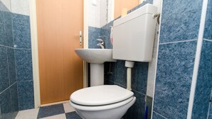 Une salle de bain avec des toilettes blanches, un lavabo et un réservoir. Les murs sont recouverts de carreaux bleus et blancs, et il y a une porte en bois.