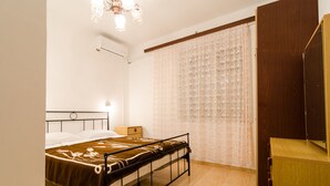 Une chambre à coucher comprenant un lit, une table de chevet, une commode en bois, une fenêtre avec des rideaux à motifs et un luminaire au plafond.