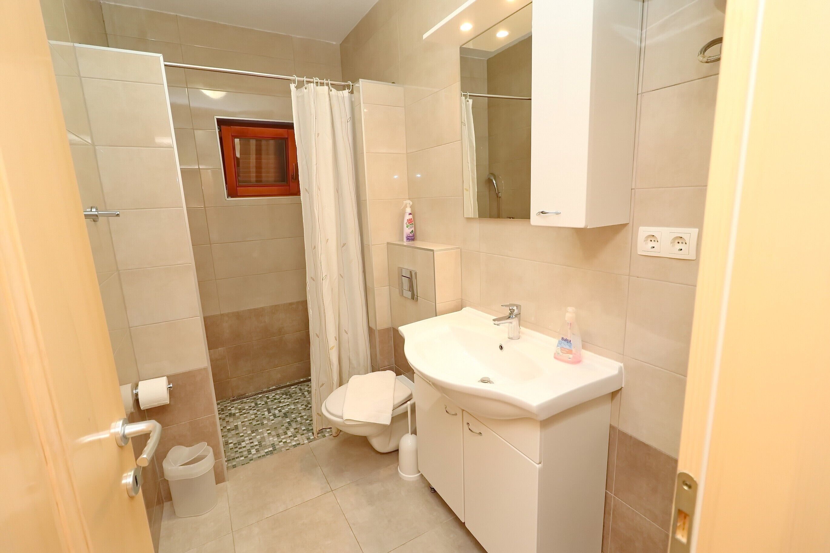 A bathroom with a shower, toilet, sink, and mirror.