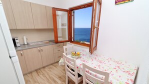 Eine kleine Küche mit Holzsäulen, einem Esstisch mit Blumenmuster und Blick auf das Meer durch ein Fenster.