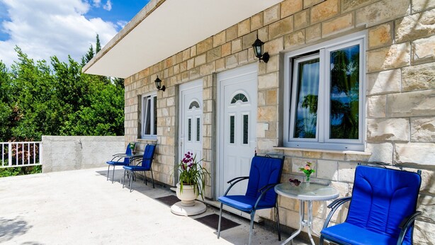 A stone building with a covered patio, two doors, and a window with a view of trees. - Apartments Versus- Studio Apartment with Terrace (Mlini)
