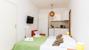A hotel room with a bed, a TV, a kitchenette, and a red chair. - Apartments Versus- Studio Apartment with Terrace (Mlini)