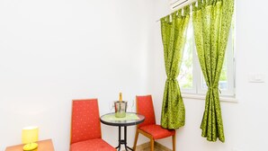 A small room with a table and two chairs, a lamp, and a window with green curtains. - Apartments Versus- Studio Apartment with Terrace (Mlini)