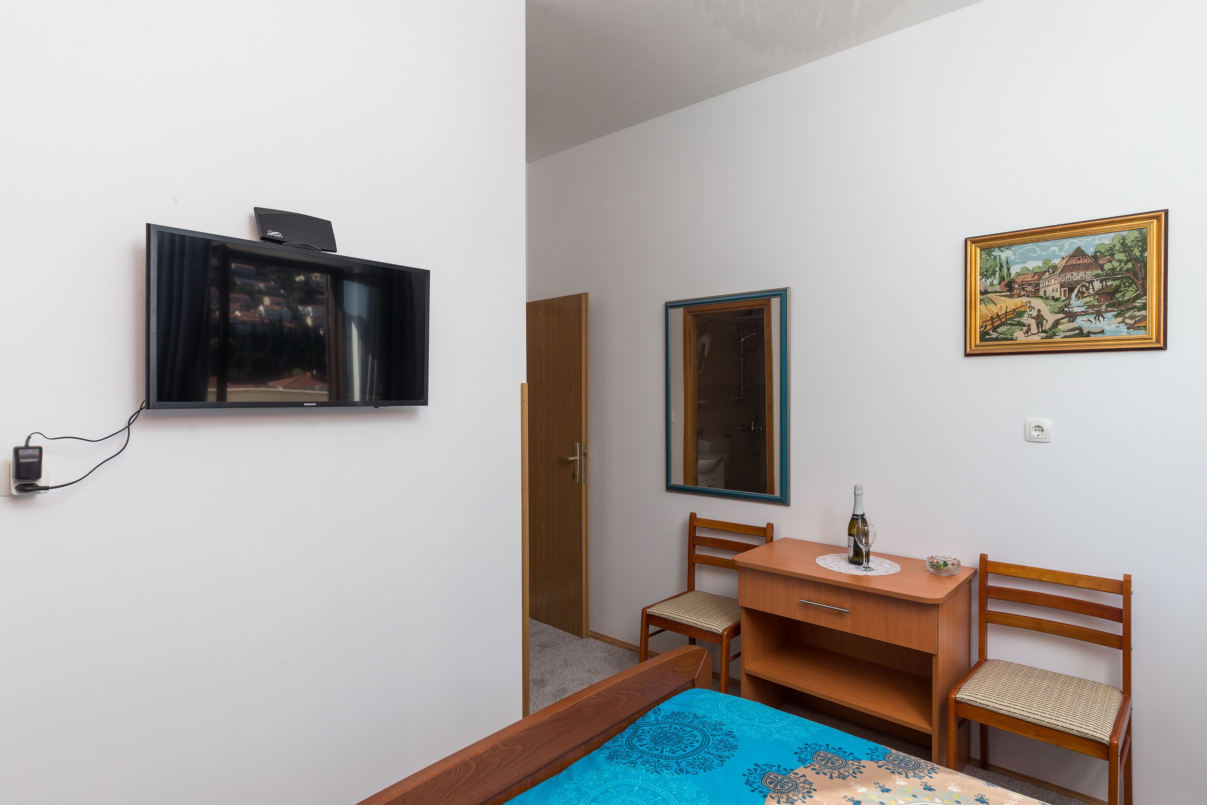 Una habitación pequeña y limpia con una cama, un escritorio, una silla, un televisor y un cuadro en la pared.