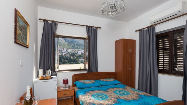 Une chambre à coucher avec un lit, une table de chevet, une table avec une bouteille et des verres, une armoire et une fenêtre avec des rideaux.