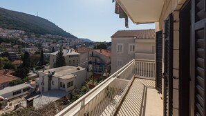 Un balcon offrant une vue sur une ville perchée sur une colline, des bâtiments aux toits recouverts de tuiles rouges et un ciel dégagé.