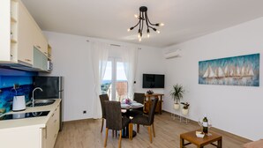 Et moderne køkken med indbygget komfur, et spiseområde med bord og stole, et fjernsyn ophængt på væggen, og et maleri af sejlbåde.