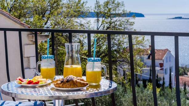 Et bord med mad og drikke på en balkon med udsigt over vand og bygninger.