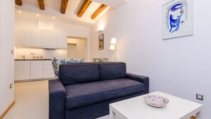 A modern living room with a dark grey sofa, a white table, and a kitchen in the background.