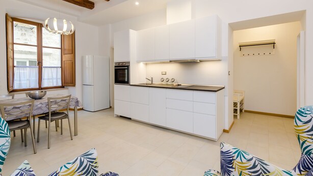 A modern kitchen with white cabinets, a built-in oven, and a dining area with a table and chairs.