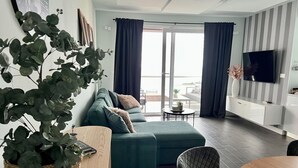 A modern living room with a sectional sofa, a dining table, and a TV mounted on the wall.