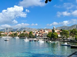 A coastal town with a marina, buildings with red roofs, and a mountain backdrop.
