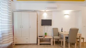 Une chambre de taille modeste, comprenant un lit, un bureau avec deux chaises, un téléviseur fixé au mur et une armoire.