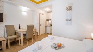 Une chambre d’hôtel avec un lit, un bureau et une chaise. Il y a une petite kitchenette dans un coin.