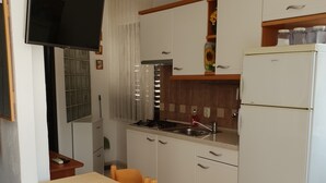 A compact kitchen with white cabinets, a built-in stove, a refrigerator, and a dining area with a table and chairs.