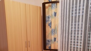 A bedroom with a wooden wardrobe, a bed with striped bedding, and a window with a floral curtain.