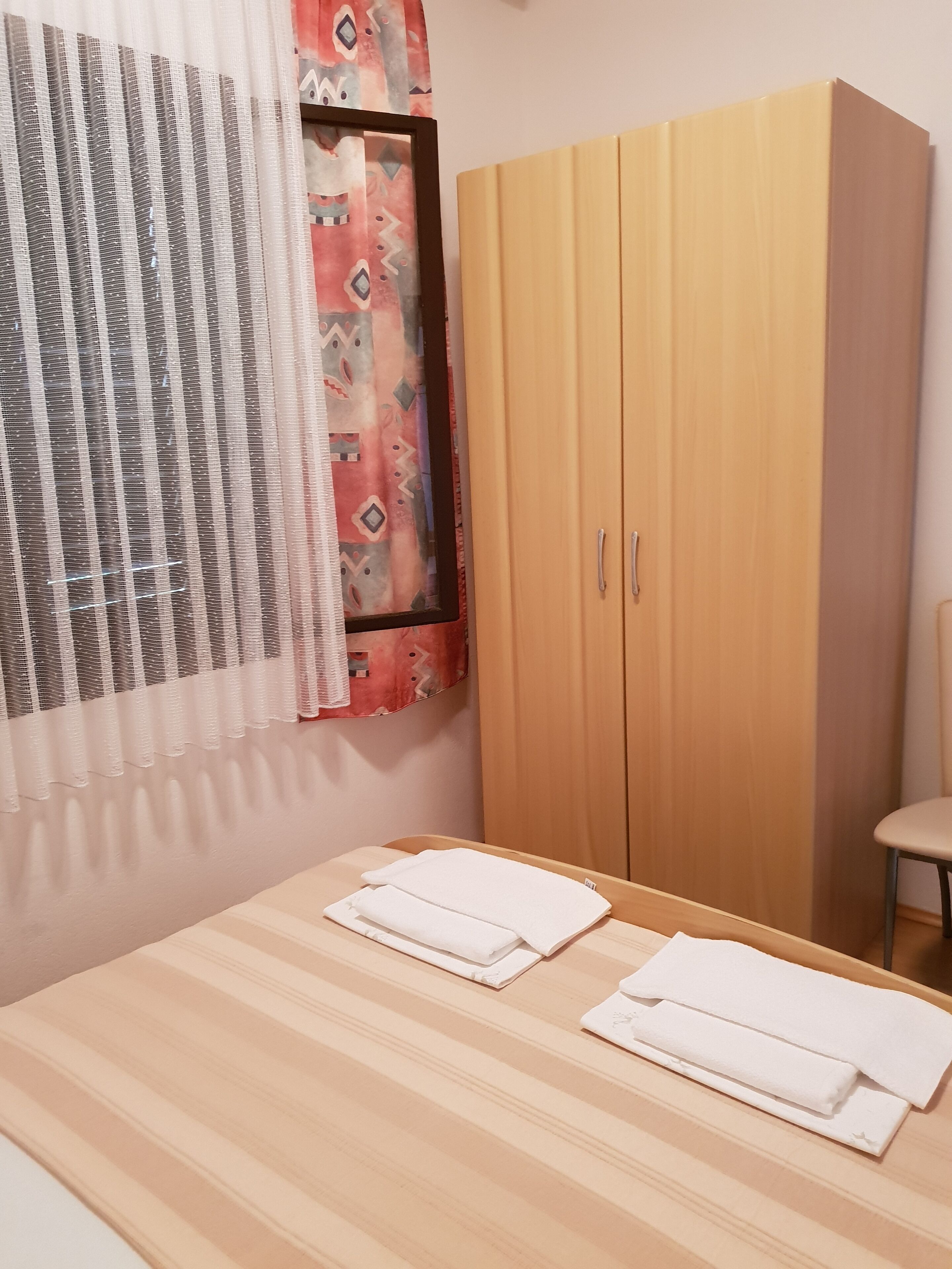A room with a wooden bed, a wardrobe, and a window with patterned curtains.