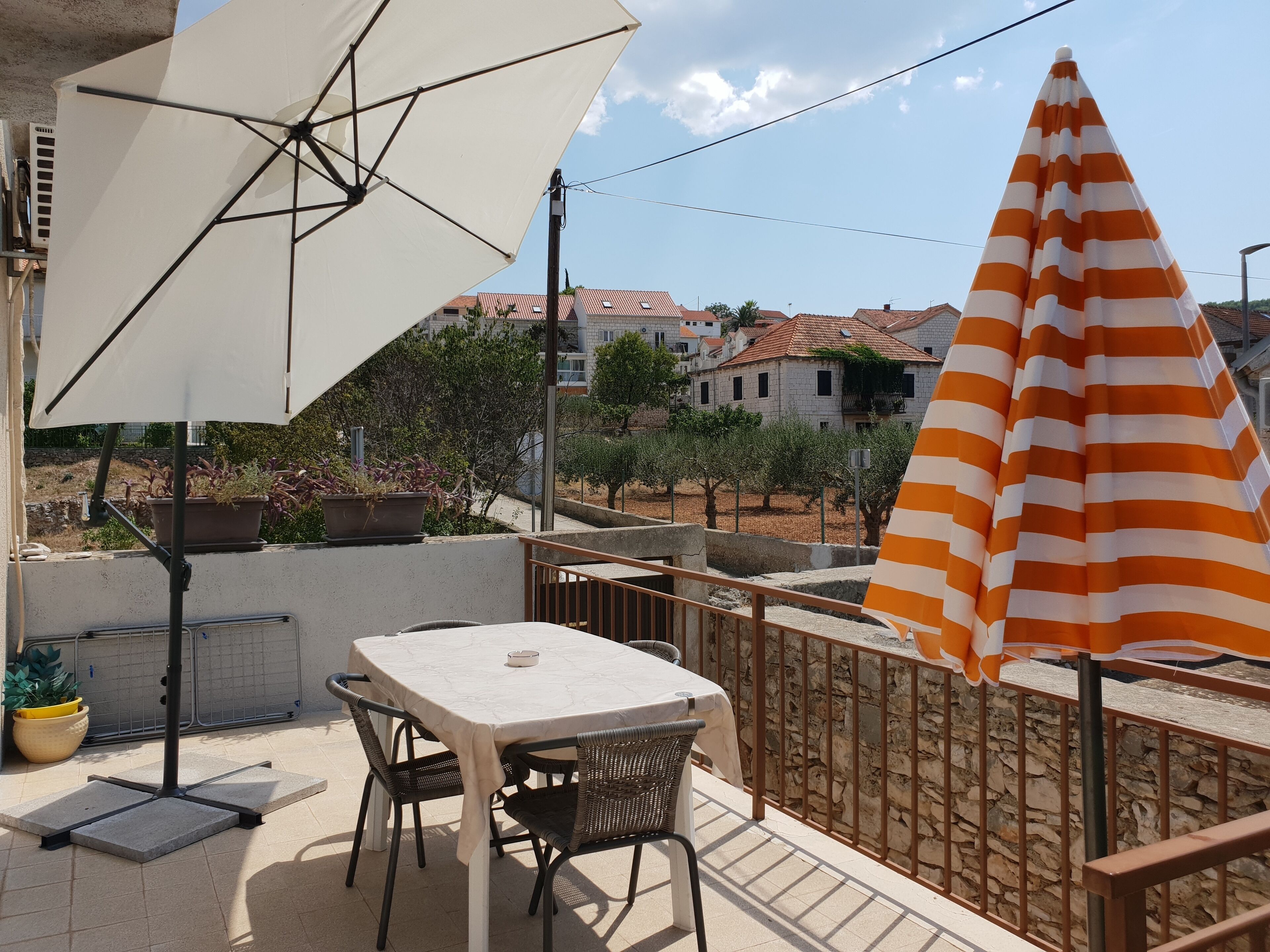 An outdoor patio with a table and chairs, a white umbrella, and a striped umbrella.