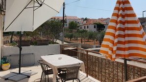 An outdoor patio with a table and chairs, a white umbrella, and a striped umbrella.
