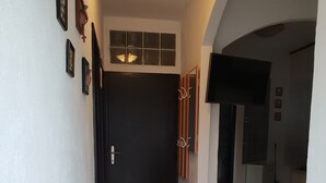 A narrow hallway leading to a dining area with a table and chairs, a black door, and a TV mounted on the wall.