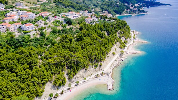 Une vue aérienne d’une ville côtière avec une plage, des maisons et une mer bleue et limpide.