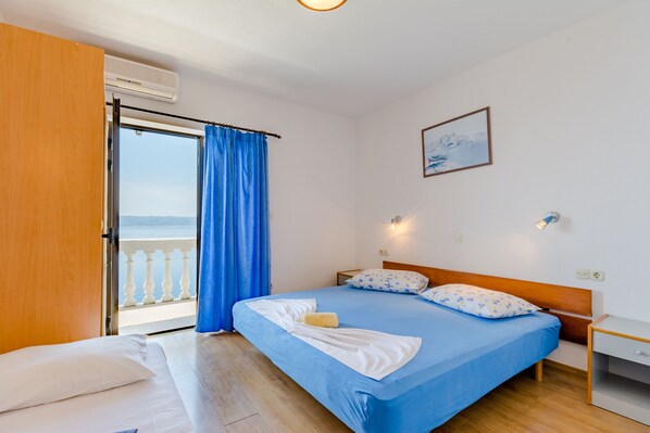 Une chambre à coucher avec un lit, une table de chevet, une fenêtre avec des rideaux bleus et une vue sur la mer.