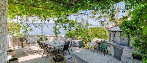A patio with a table and chairs, a stone wall, and a view of the sea.