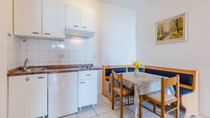 Une cuisine compacte avec des meubles blancs, un évier et un coin repas comprenant une table et un banc.