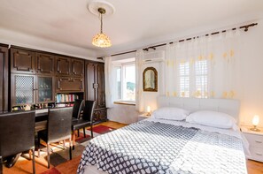 Une chambre à coucher avec un lit, un bureau et une chaise. Il y a une fenêtre avec des rideaux et un miroir au mur.