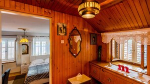 Ein Zimmer aus Holz mit einem Bett, einem Schminktisch, einem Spiegel und einem Fenster mit Spitzenvorhängen.