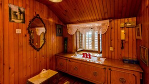 Ein Holzblockhaus-Innenraum mit einem Holzkleiderschrank, einem Spiegel, einem Fenster mit Spitzenvorhängen und einem kleinen Tisch mit einer Handtasche.