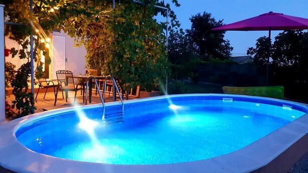 Een buitenzwembad met een helder, blauw watergedeelte, omringd door een patio met stoelen en een tafel.