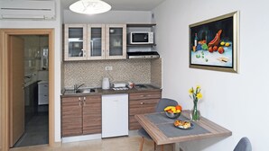 Eine kompakte Küche mit Holdekor-Schränken, einer Mikrowelle und einem Geschirrspüler. Ein Esstisch mit Blumenvase und Obstschale.