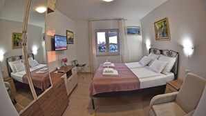 Ein Hotelzimmer mit zwei Betten, einem großen Spiegel, einem Fernseher, einem Fenster mit Vorhängen und Bildern an den Wänden.