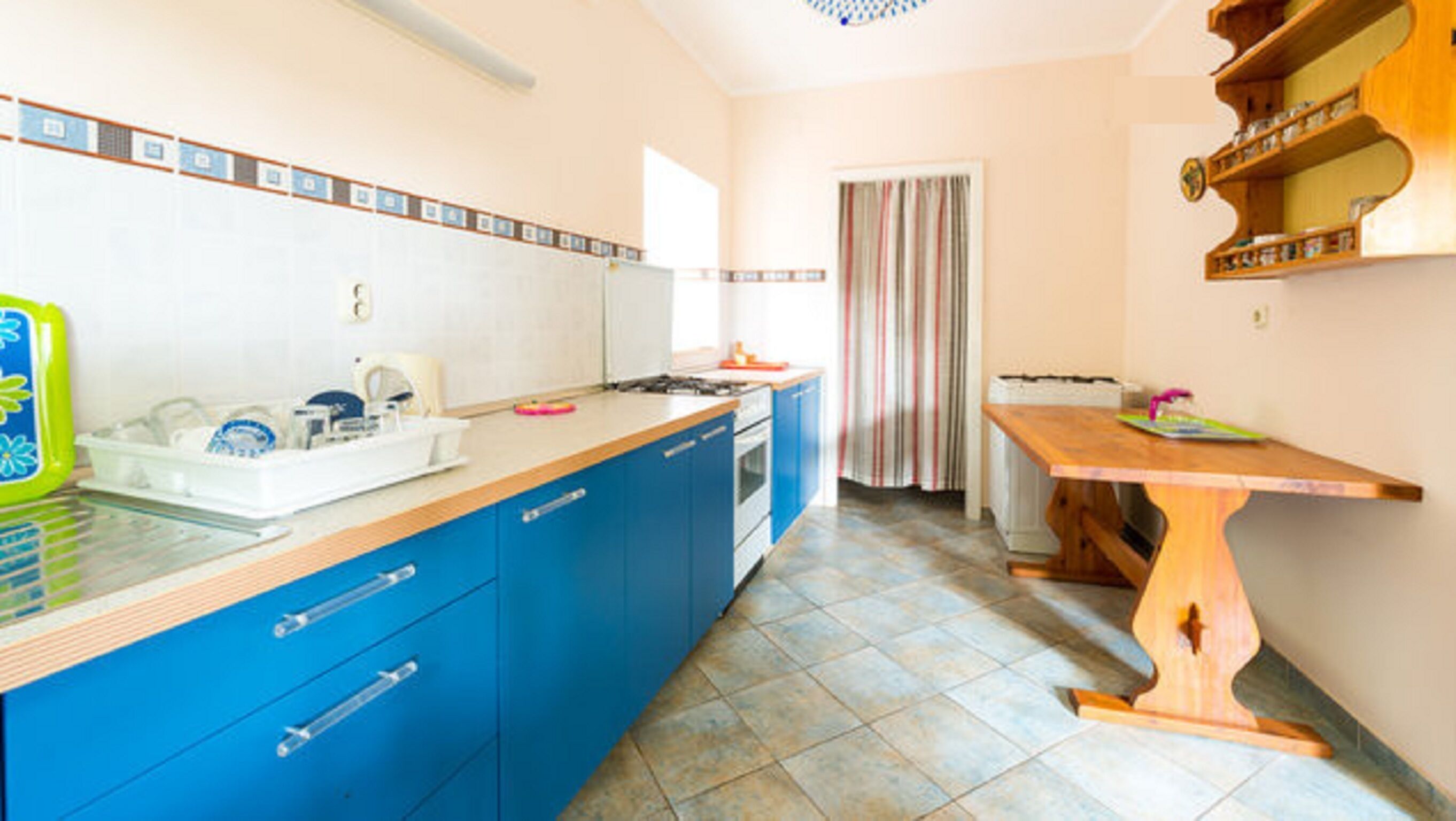 Una cucina con mobili azzurri, un tavolo di legno e un pavimento piastrellato.