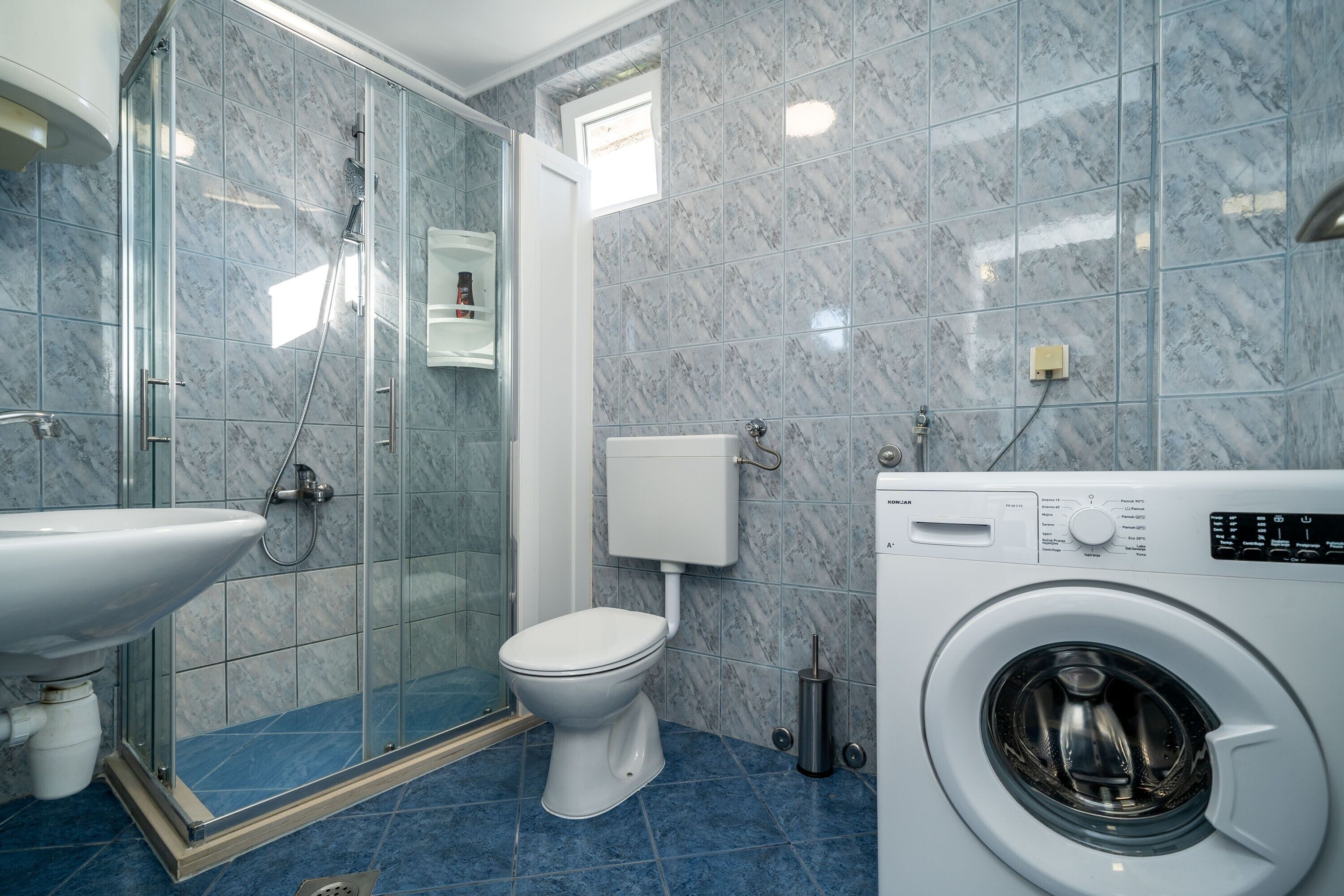 Une salle de bain moderne avec une douche à parois de verre, des toilettes, un lavabo et un lave-linge à chargement frontal.