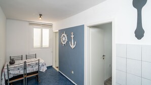 A room with a dining table, chairs, a window with blinds, a wall with nautical decorations, and a door leading to another room.