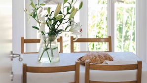 A wooden dining table with a white tablecloth, two wooden chairs, a vase with white flowers, and a loaf of bread on the table. - Apartments Bonavista - Superior Two Bedroom Apartment with Balcony and Sea View (A1) (Dubrovnik)