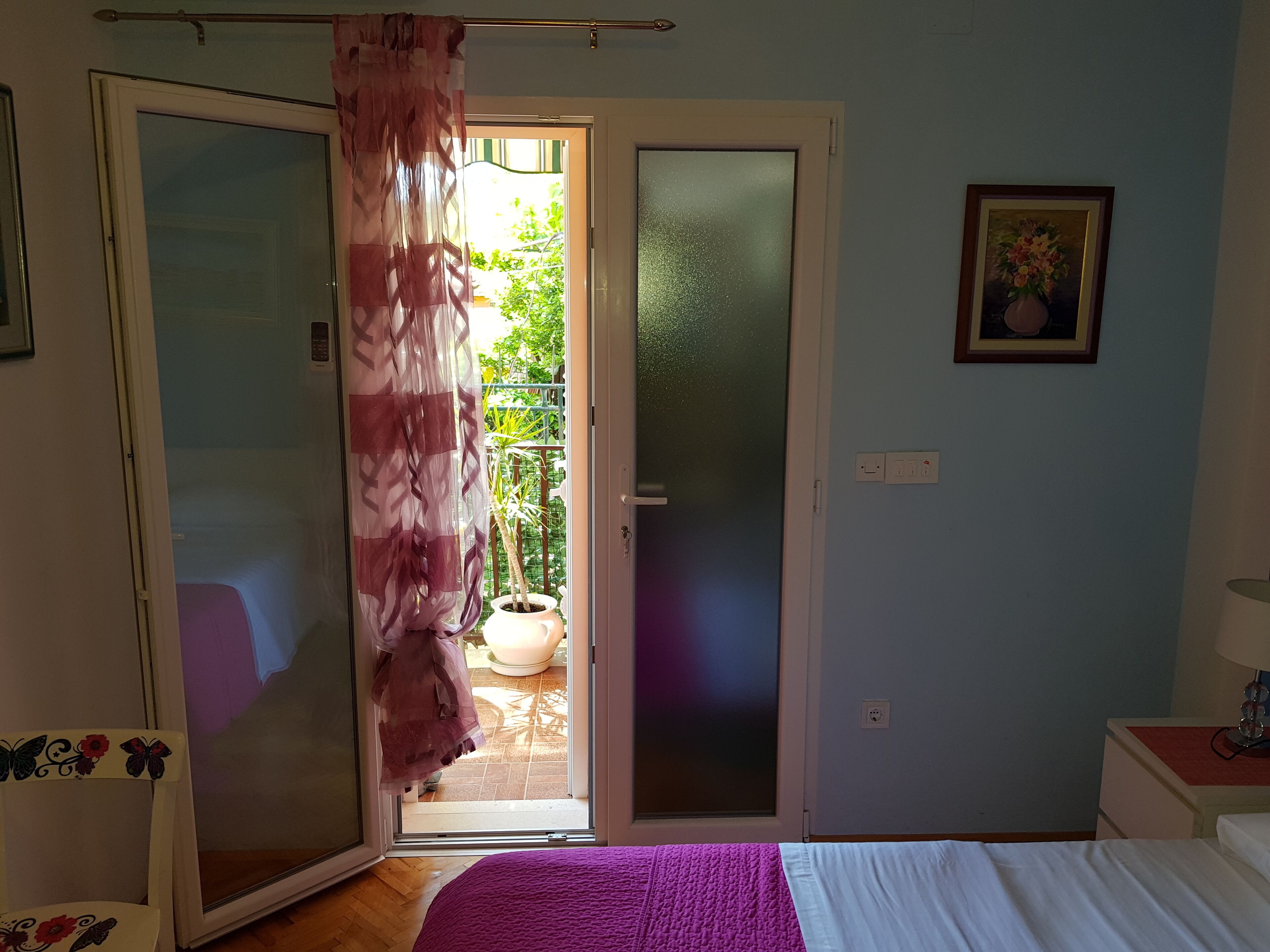 A bedroom with a bed, a sliding glass door leading to a balcony, and a small bedside table with a lamp.