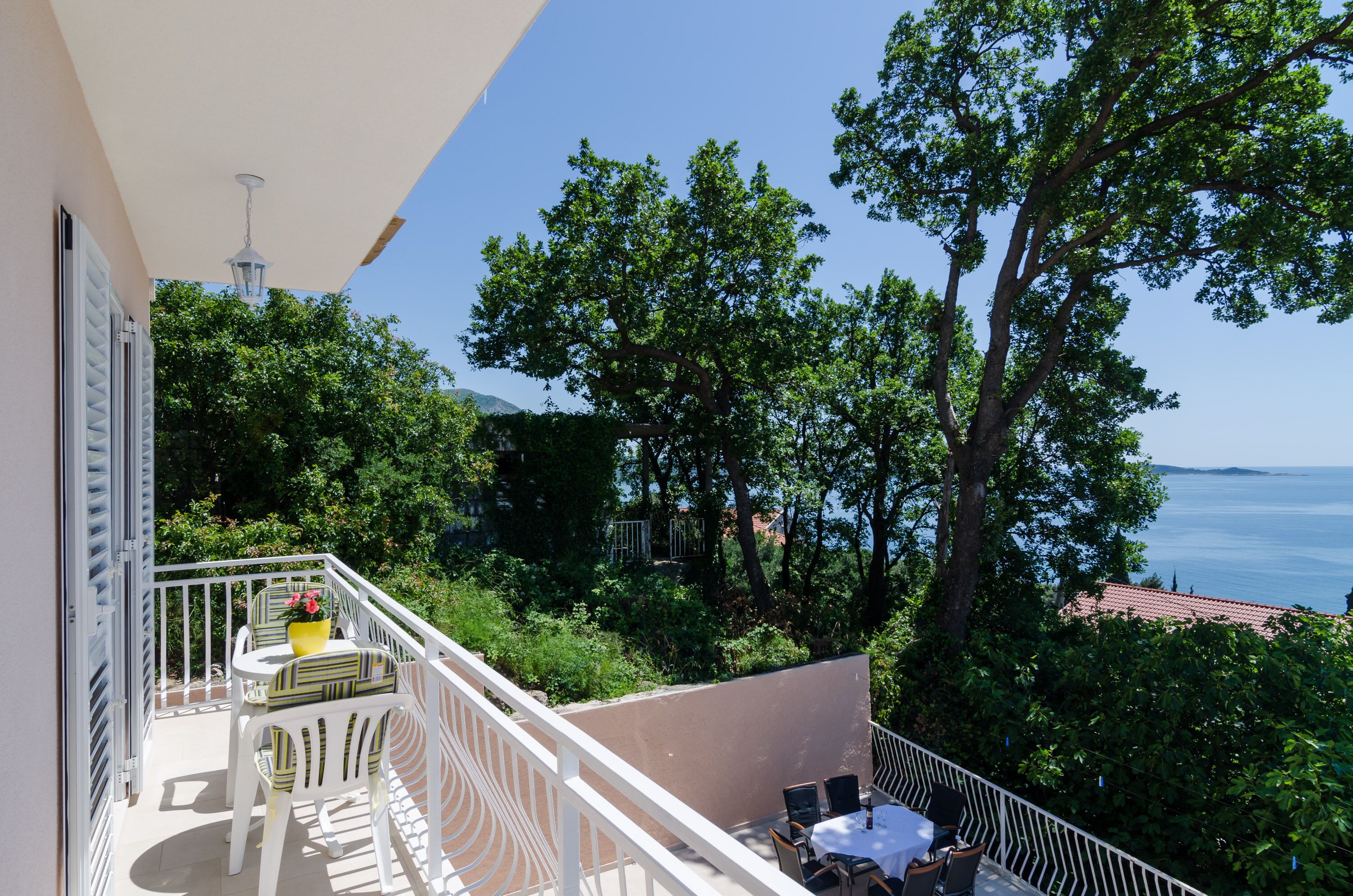 A balcony with a table and chairs, overlooking a lush green landscape and the sea.