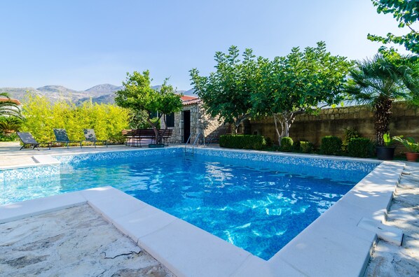 A rectangular swimming pool with clear blue water, surrounded by a stone wall and lush greenery.