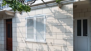 A building with a white door, a window with white shutters, and a tiled ground. - Katarina rooms - twin room (Dubrovnik)