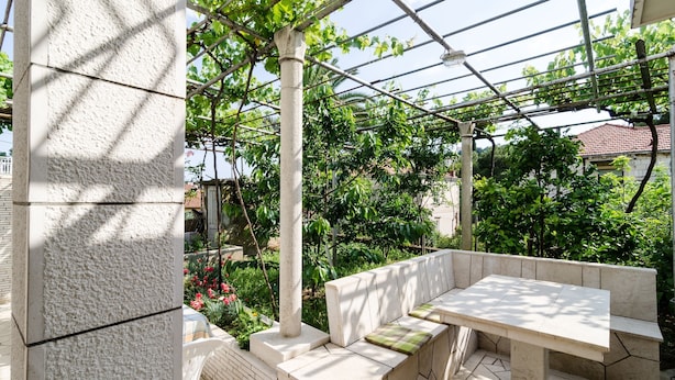 A covered outdoor seating area with a table and benches, surrounded by greenery and a pergola structure. - Katarina rooms - twin room (Dubrovnik)